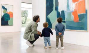 Un genitore osserva un dipinto insieme a due bambini piccoli in un museo.