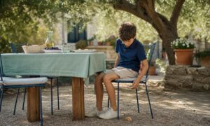 Bambino seduto composto osserva un pezzo di pane caduto sotto il tavolo.