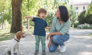 Bambino indica un cane e gesticola mentre il genitore lo ascolta sorridendo.
