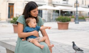 Bambino indica un piccione mentre il genitore segue con attenzione il suo gesto.