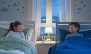 Due bambini a letto si guardano in silenzio nella luce blu della sera.