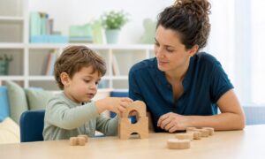 Bambino costruisce una struttura in legno mentre la logopedista incoraggia il dialogo.