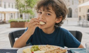 Bambino mastica lentamente una mela durante un pranzo all'aperto in una piazza italiana.